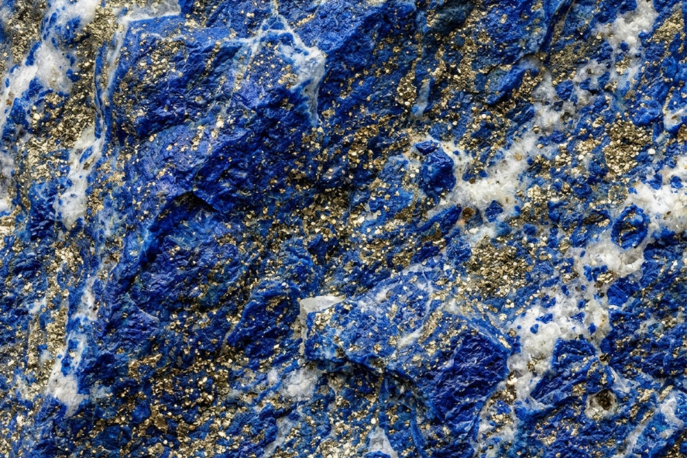 Detailaufnahme eines Lapislazuli-Gesteins, das tiefblaue Bereiche mit goldenen Pyrit-Einschlüssen und weißen Calcit-Adern zeigt. Die Oberfläche ist rau und strukturiert.