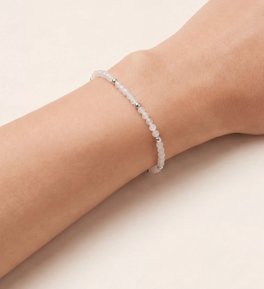 Zartes, elegantes Perlenarmband mit kleinen, schimmernden weißen Edelsteinperlen und glänzenden silbernen Akzenten, stilvoll am weiblichen Handgelenk getragen, präsentiert vor einem hellen Hintergrund. Ein minimalistisches und vielseitiges Schmuckstück.