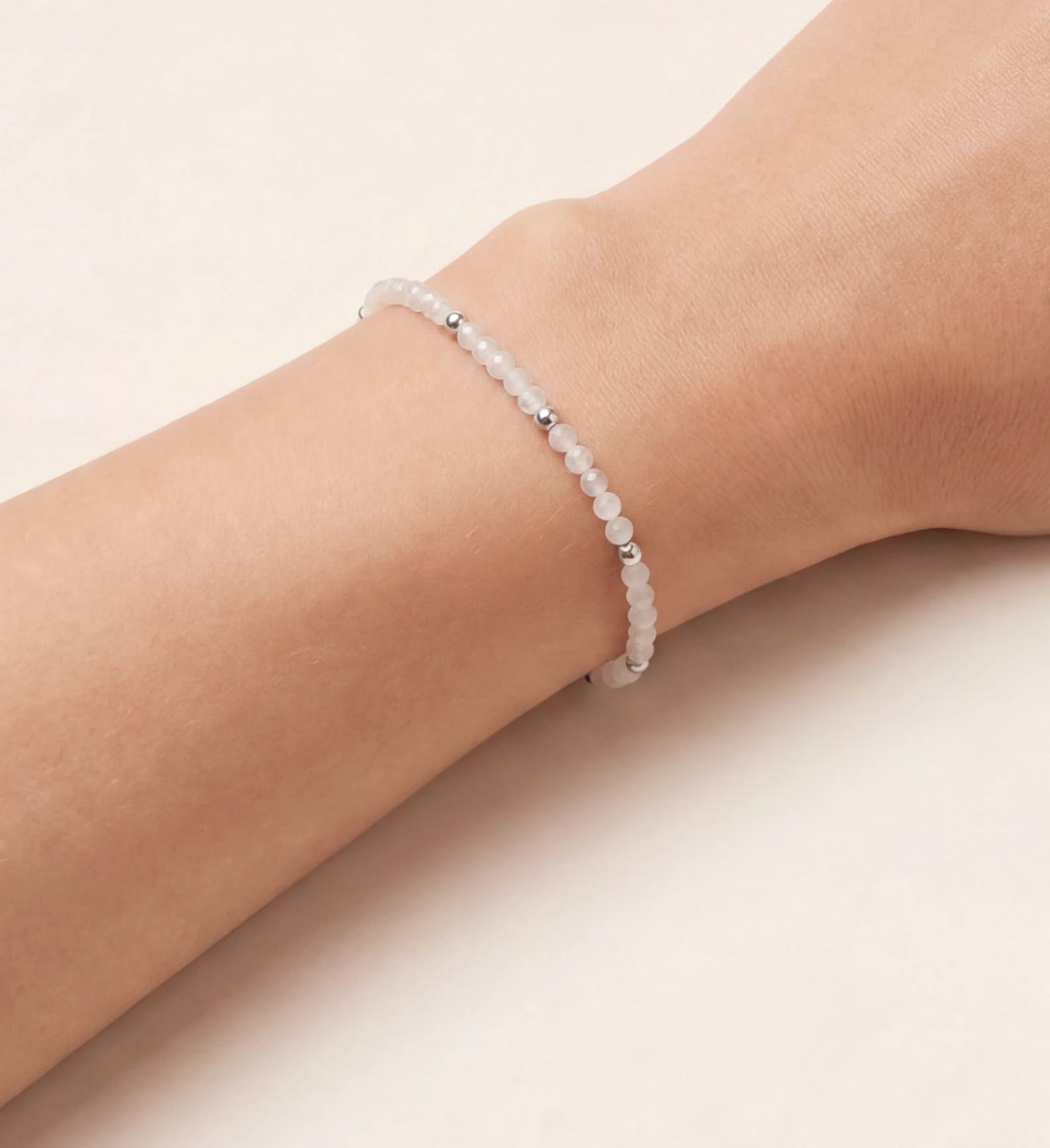 Zartes, elegantes Perlenarmband mit kleinen, schimmernden weißen Edelsteinperlen und glänzenden silbernen Akzenten, stilvoll am weiblichen Handgelenk getragen, präsentiert vor einem hellen Hintergrund. Ein minimalistisches und vielseitiges Schmuckstück.